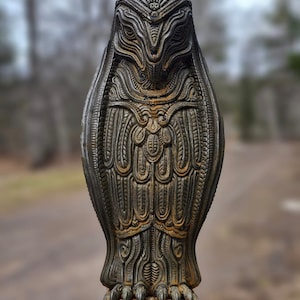 May include: A detailed, intricately carved owl statue with a rusty brown finish. The owl is standing on a base with claws and has a detailed face with large eyes.