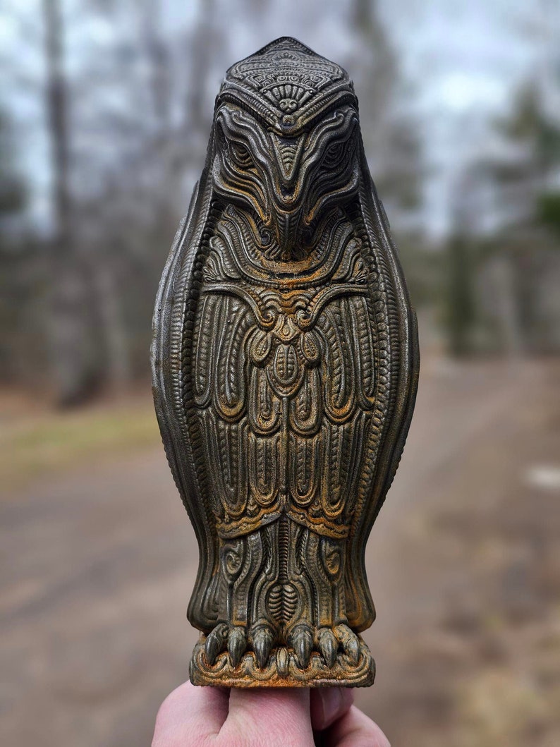 May include: A detailed, intricately carved owl statue with a rusty brown finish. The owl is standing on a base with claws and has a detailed face with large eyes.