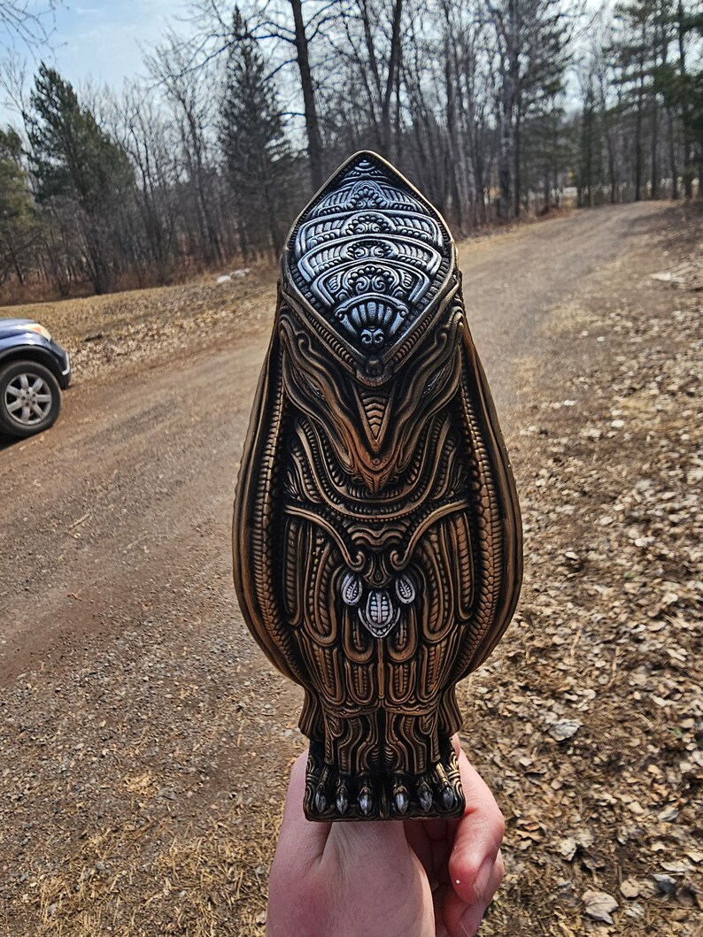 May include: A detailed, intricately carved, gold-coloured owl sculpture with silver accents. The owl is standing on a pair of feet with claws.
