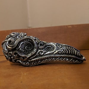 May include: A silver-toned, ornate, bird skull-shaped ring with intricate details.