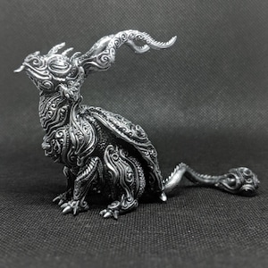 Peut inclure: Une figurine argentée en forme de dragon, aux détails complexes, avec une longue queue recourbée et des cornes. La figurine est posée sur une surface noire.
