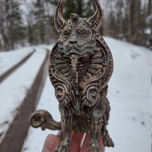 May include: A detailed, intricately sculpted bronze figurine of a mythical creature with horns, a long snout, and a curled tail. The figurine is painted in shades of green and brown, giving it an aged and weathered look.