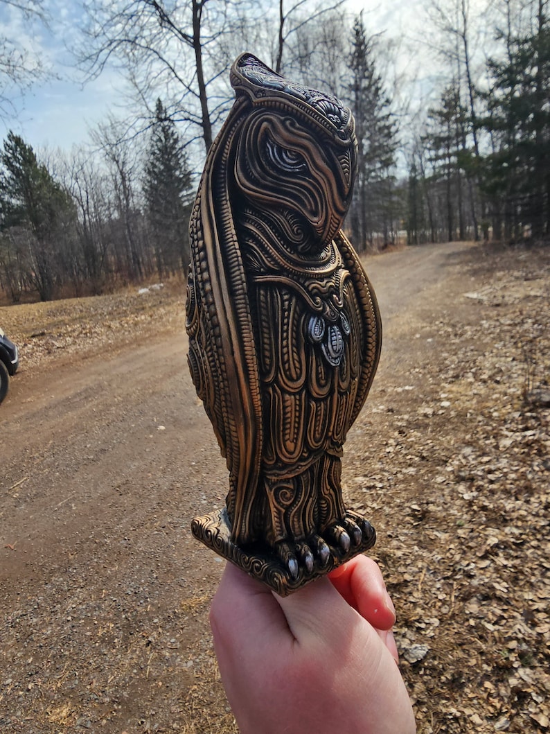 May include: A detailed, intricately carved owl sculpture with a gold and silver finish. The owl is standing on a square base with intricate carvings.