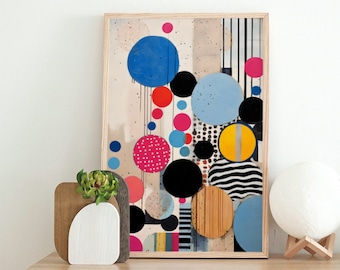 May include: A framed abstract art print with a colorful geometric pattern of overlapping circles in shades of blue, pink, yellow, black, and white. The print is displayed on a white dresser with a wooden top, a small potted plant, and a white moon-shaped lamp.