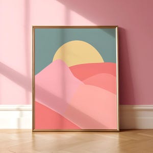 May include: A framed abstract print of a pink and orange landscape with a yellow sun in a blue sky. The frame is gold.