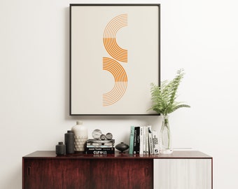 May include: A mid-century modern sideboard with two sliding doors, one with a dark wood finish and the other with a light wood finish. The sideboard is decorated with a framed print of an abstract geometric design in orange and white, a vase of green ferns, and a collection of books and decorative objects.
