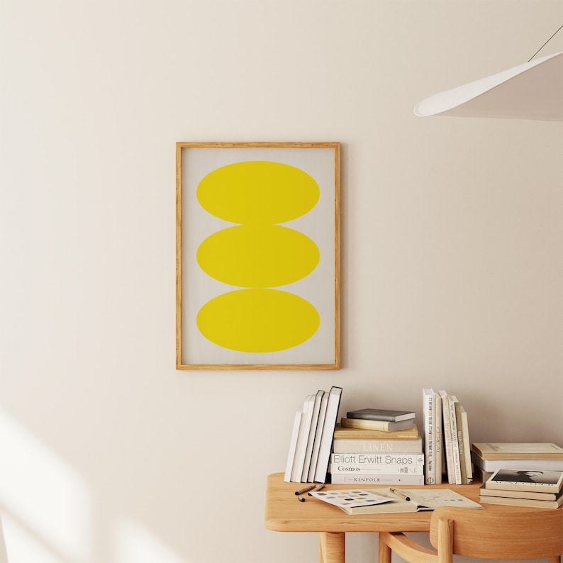 May include: A framed print with a minimalist design featuring three stacked yellow ovals on a white background.