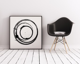 May include: Black and white abstract art print with concentric circles in a square frame, hanging on a white wall next to a black chair with wooden legs.