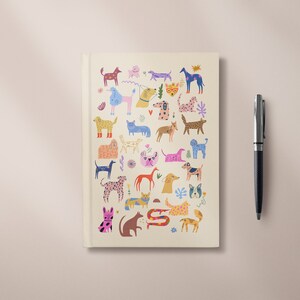 May include: A cream-colored notebook with a colorful illustration of various dogs on the cover. The dogs are depicted in different poses and styles, with a variety of colors and patterns.