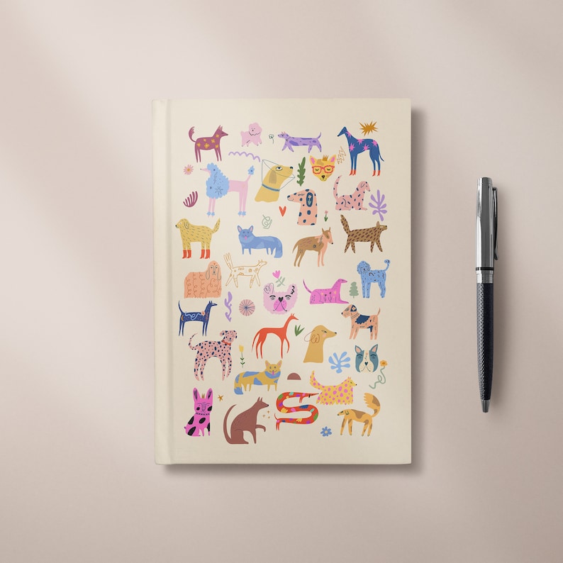 May include: A cream-colored notebook with a colorful illustration of various dogs on the cover. The dogs are depicted in different poses and styles, with a variety of colors and patterns.