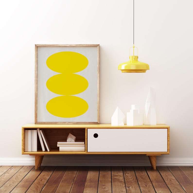 May include: A wooden media console with a white drawer and open shelves. The console has a yellow lamp hanging above it and a framed print with three yellow circles on a gray background.
