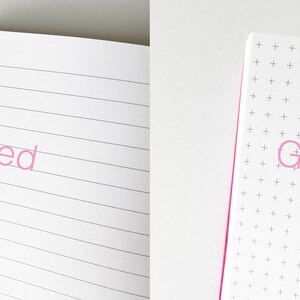 May include: Close-up of two open notebooks. The left notebook has lined pages and the word "Lined" printed in pink. The right notebook has graph paper and the word "Graph" printed in pink.