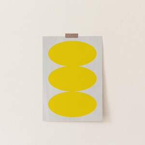 May include: A print with three stacked yellow ovals on a white background.