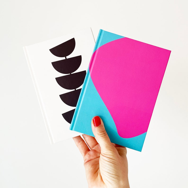 May include: Two notebooks, one with a black and white geometric design and the other with a pink and blue abstract design.