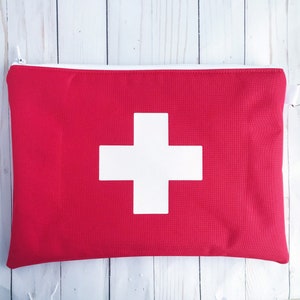 Puede incluir: Bolsa roja con cremallera con un signo m&aacute;s blanco en la parte delantera. La bolsa est&aacute; hecha de tela y tiene una cremallera.