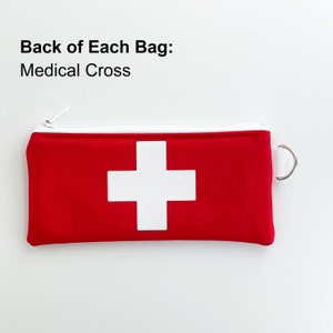 Op de afbeelding: Rode ritszak met een wit medisch kruis op de voorkant. De tekst "Back of Each Bag: Medical Cross" staat boven de tas.