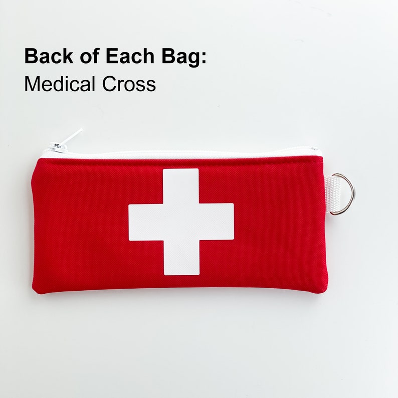 Op de afbeelding: Rode ritszak met een wit medisch kruis op de voorkant. De tekst "Back of Each Bag: Medical Cross" staat boven de tas.