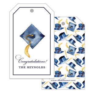 May include: White graduation gift tags with a navy blue mortarboard and gold tassel design. One tag reads "Congratulations! The Reynolds." The other tag has a pattern of navy blue graduation caps and gold feathers.