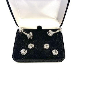 May include: A set of silver cufflinks and shirt studs in a black velvet box. The cufflinks and studs feature a knot design.