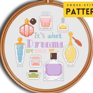 Puede incluir: Patrón de punto de cruz con una variedad de botellas y frascos de perfume en rosa, azul, amarillo y verde. El texto "It's what Dreams are made of..." está incluido en el diseño.