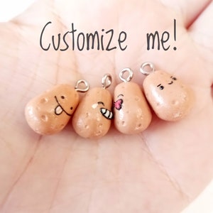 May include: Four small, brown, clay potato charms with different facial expressions. Each charm has a silver loop for hanging. The charms are on a hand with the text "Customize me!" written above them.