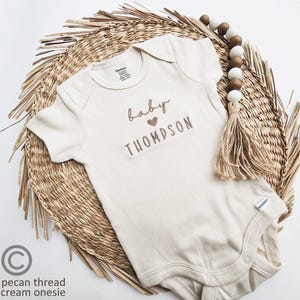 A baby onesie with the name "Baby Thompson" printed on it, placed on a woven placemat.
