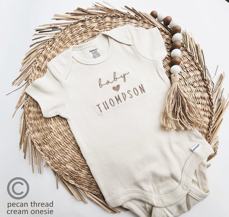 A baby onesie with the name "Baby Thompson" printed on it, placed on a woven placemat.