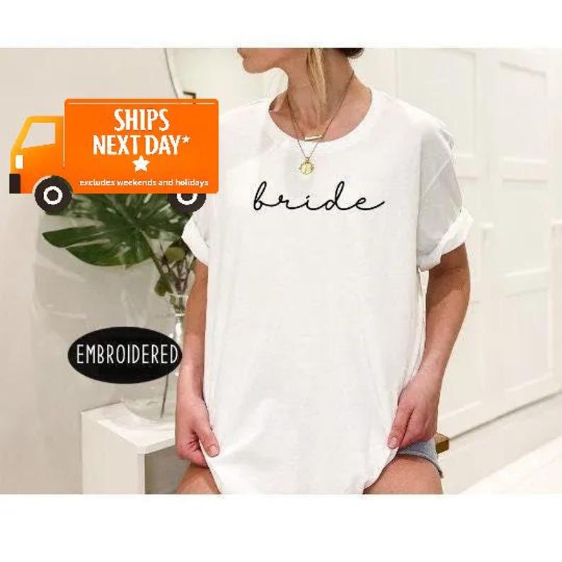A person wearing a white t-shirt with the word "Bride" printed on it, standing in front of a white wall.