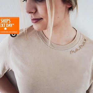 A woman wearing a beige t-shirt with the word "mama" embroidered on it.