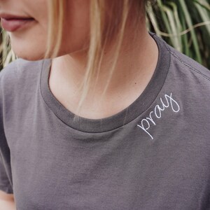 A close-up of a person wearing a gray t-shirt with the word "pray" written on it.