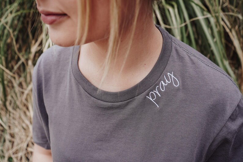A close-up of a person wearing a gray t-shirt with the word "pray" written on it.