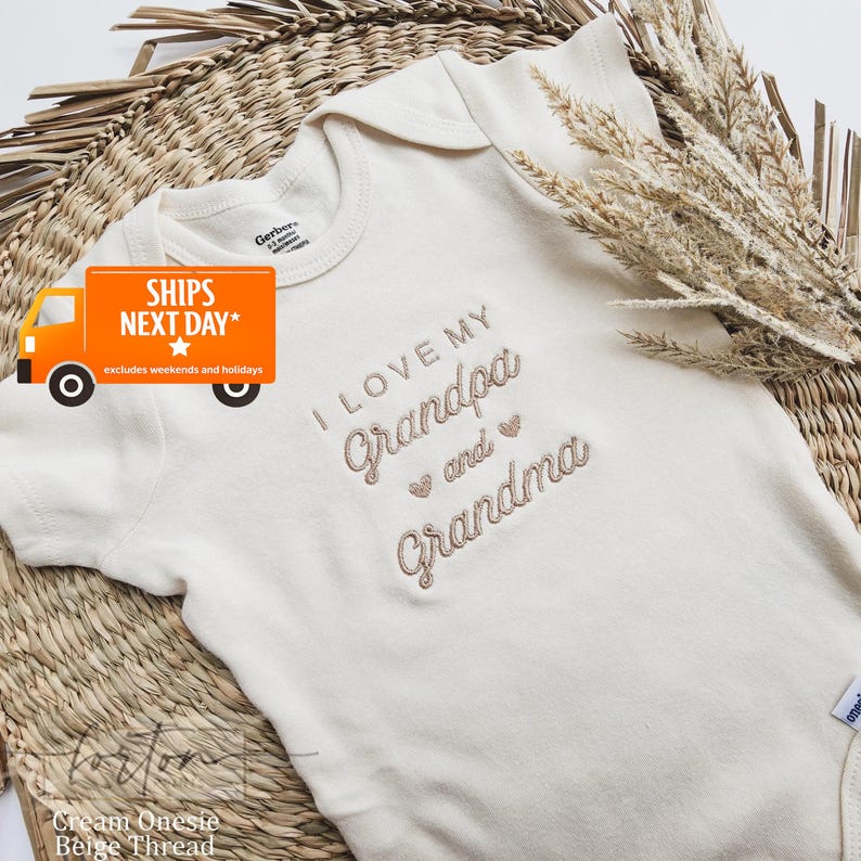 A white baby onesie with the text "I LOVE MY GRANDMA and GRANDMA" embroidered on it, placed on a woven basket. There is also a shipping label with the text "SHIPS NEXT DAY" and an orange truck icon, indicating that the item is being shipped.