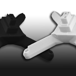 Könnte beinhalten: Zwei 3D-gedruckte Drohnenrahmen, einer schwarz und einer weiß. Beide Rahmen haben vier Arme und eine zentrale Plattform mit einem Stecker.