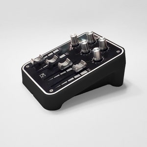 Op de afbeelding: Een zwart PC-paneel met zilveren knoppen en schuifregelaars. Het paneel heeft een rechthoekige vorm met afgeronde randen en een zilveren rand. De knoppen en schuifregelaars zijn op het bovenoppervlak van het paneel geplaatst.