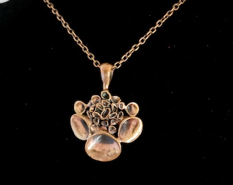May include: A bronze necklace with a pendant featuring a cluster of small, round, green stones surrounded by larger, smooth, bronze shapes.