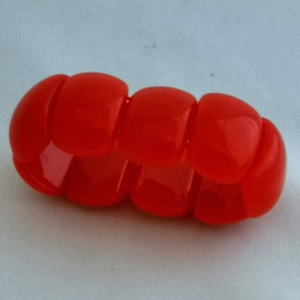 May include: A bright red plastic bracelet made of multiple connected square beads.