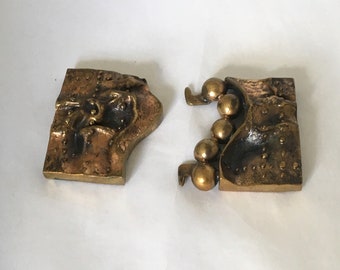 Peut inclure: Fermoir en deux parties de couleur bronze avec une surface texturée. Une pièce présente un visage sculpté, l'autre une série de sphères attachées. Le fermoir est conçu pour relier les deux pièces.
