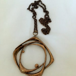 May include: A vintage copper-coloured necklace with a geometric pendant. The pendant has an open, layered design with a circular centre and two small spheres. The chain is a matching dark brown colour.