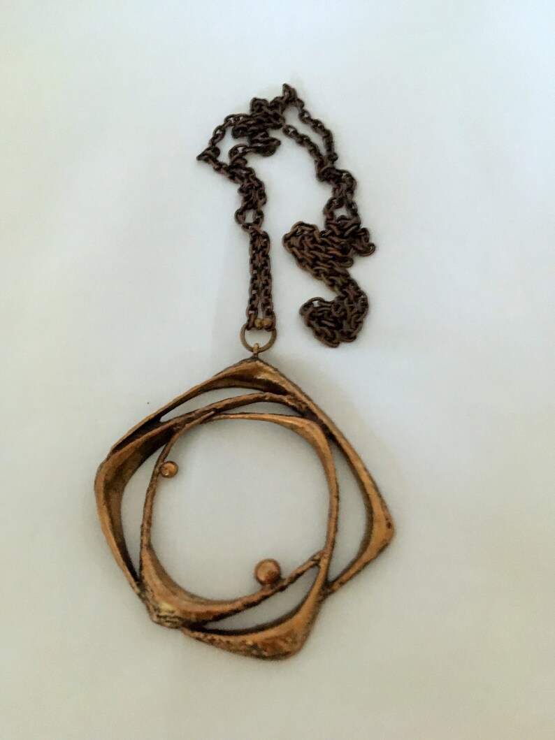 May include: A vintage copper-coloured necklace with a geometric pendant. The pendant has an open, layered design with a circular centre and two small spheres. The chain is a matching dark brown colour.