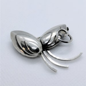 Peut inclure: Un charme en argent en forme d'insecte stylisé avec un corps arrondi et de longues pattes fines. Le charme a une boucle en haut pour l'attacher à un bracelet ou un collier.