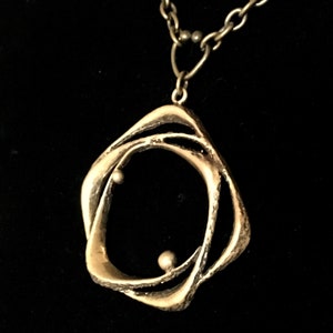 May include: A silver pendant necklace with an abstract, interwoven design. The pendant has an open shape with two small, spherical accents. The chain is silver, and the background is black.