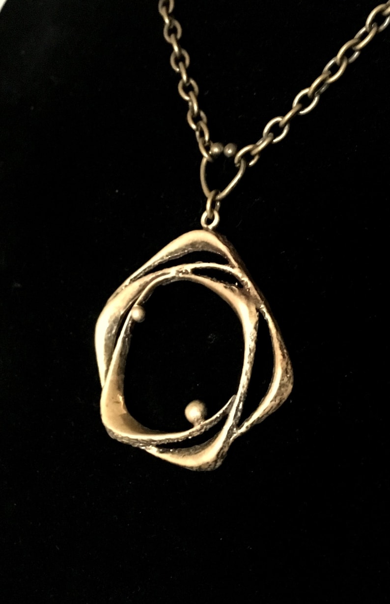 May include: A silver pendant necklace with an abstract, interwoven design. The pendant has an open shape with two small, spherical accents. The chain is silver, and the background is black.