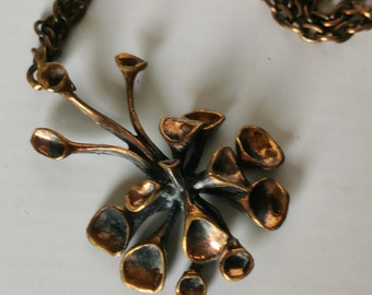 May include: A vintage bronze-toned necklace featuring a pendant with a cluster of stylized, petal-shaped elements. The pendant is attached to a matching chain. The design has a botanical or organic aesthetic, with a dark patina and highlights of gold.