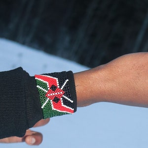Può includere: Un braccio che indossa una camicia nera a maniche lunghe con un braccialetto di perline nei colori della bandiera del Kenya.