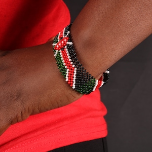 Può includere: Un braccialetto di perline con i colori della bandiera del Kenya. Il braccialetto è realizzato con perline verdi, nere, rosse e bianche.