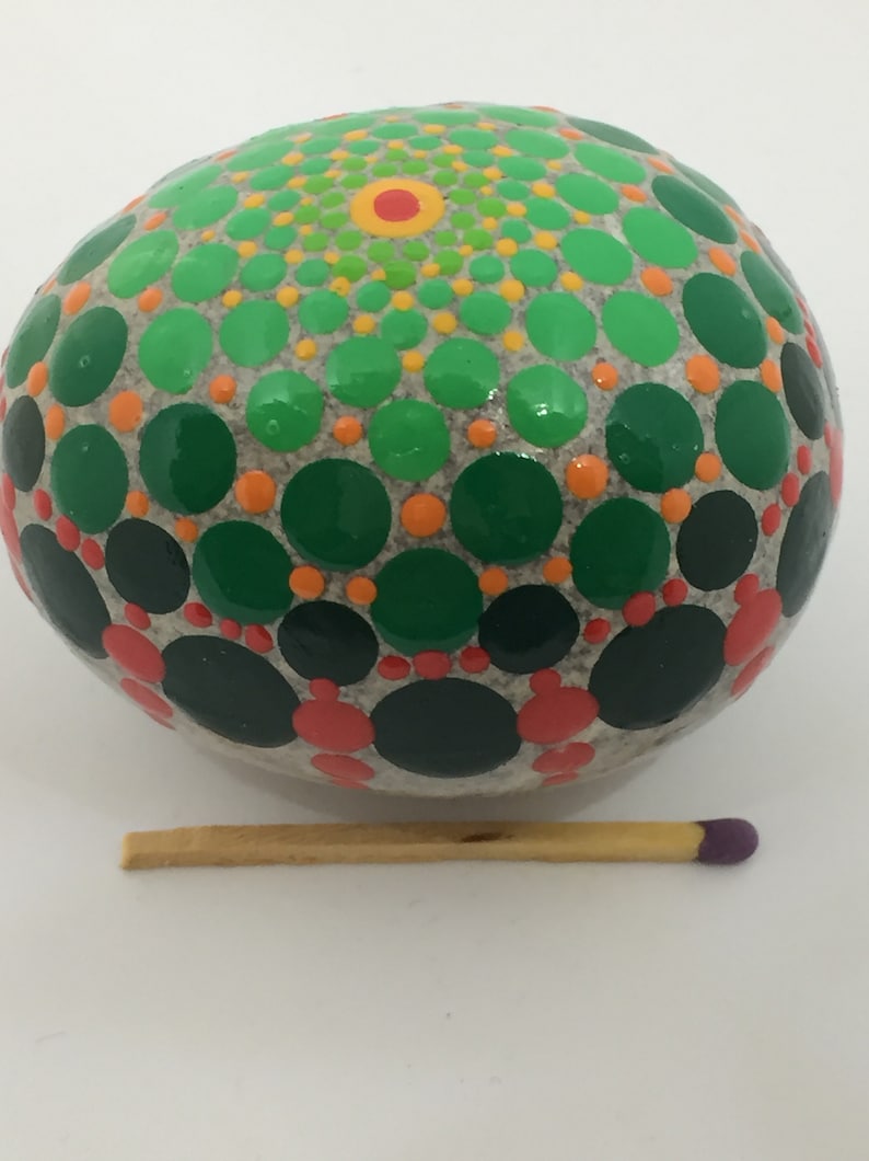 May include: A round, gray stone painted with a mandala design in shades of green, orange, and red. The stone is about the size of a matchstick.