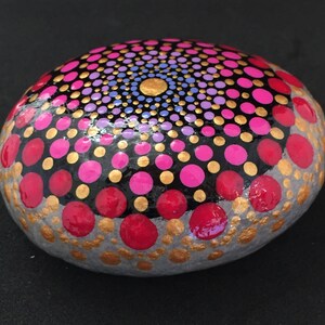 May include: A gray stone painted with a mandala design in shades of pink, red, gold, and purple.