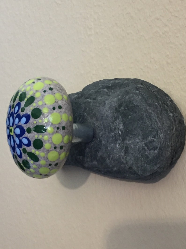 May include: A painted rock mushroom with a green, yellow, blue and white mandala design. The mushroom is attached to a gray rock base.