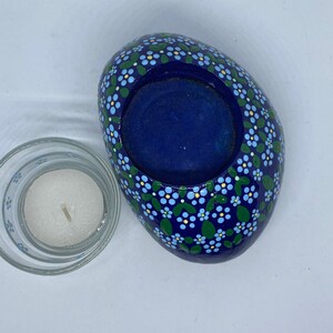 Puede incluir: Un portavelas de piedra azul con un dise&ntilde;o floral blanco y verde. El portavelas tiene una forma redonda, ligeramente ovalada, y un centro hueco para una vela de t&eacute;.