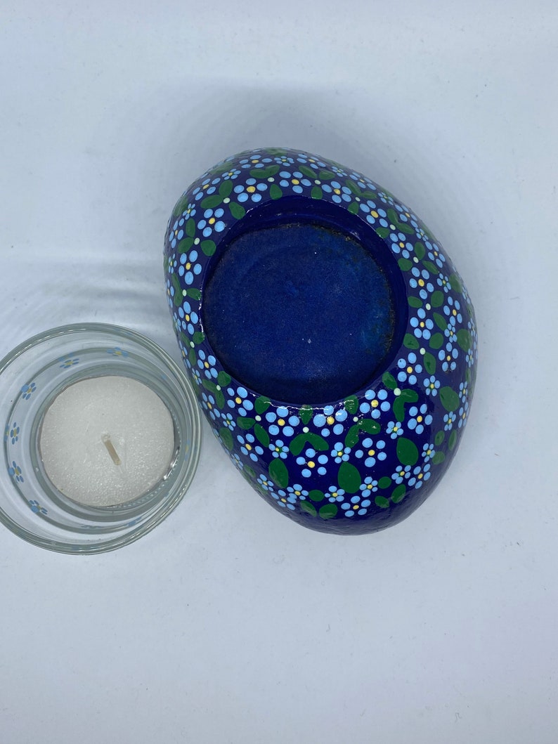 Puede incluir: Un portavelas de piedra azul con un dise&ntilde;o floral blanco y verde. El portavelas tiene una forma redonda, ligeramente ovalada, y un centro hueco para una vela de t&eacute;.